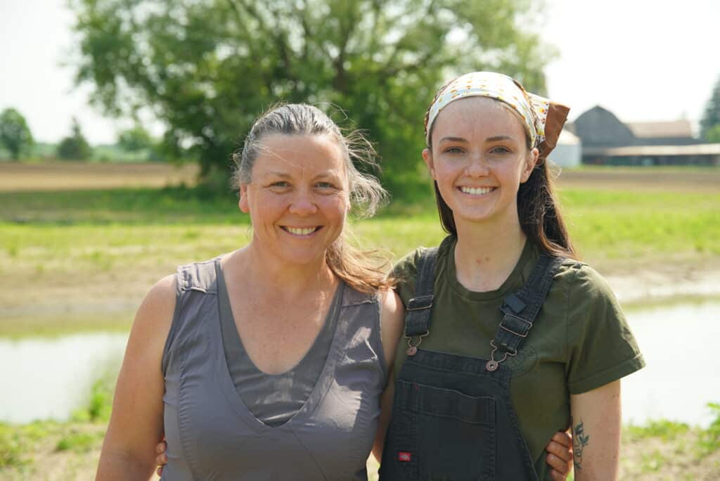 Two women smile in front of fields.