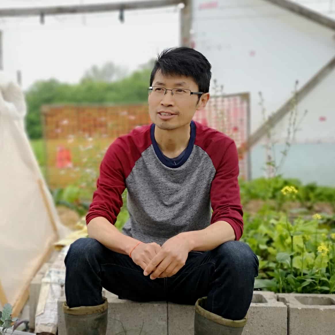 A young man sitting on a brick wall in a greenhouse on an Ontario farm.