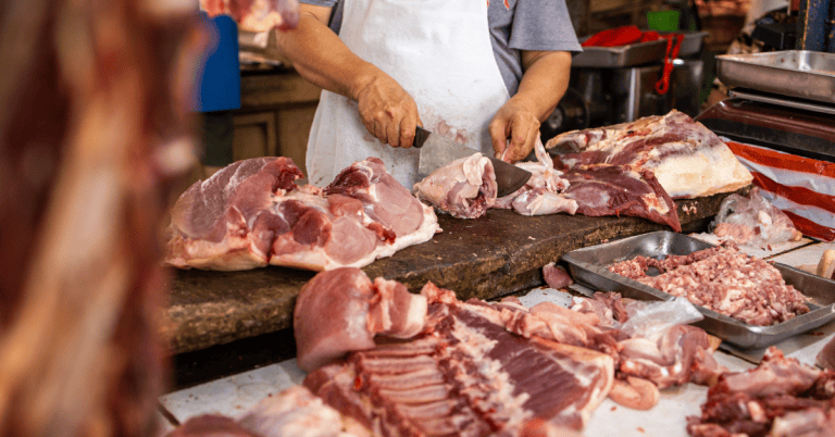 A man is slicing meat on a butcher's block.