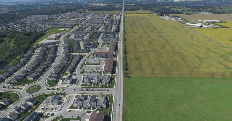 An aerial view of a residential area (left) and farmland (right) split by a road.