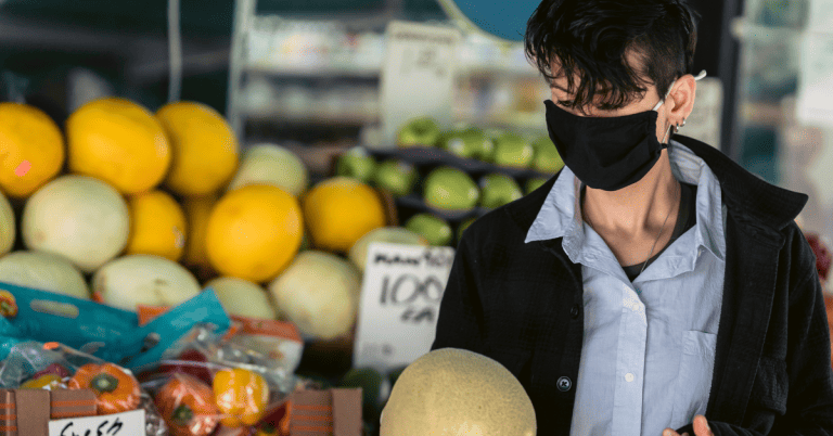 A person wearing a face mask shopping for produce in a store.