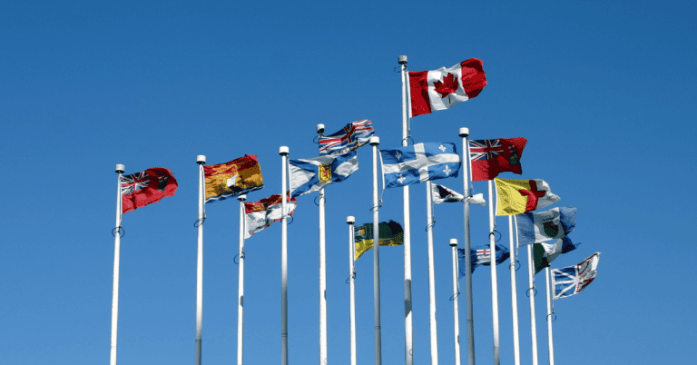 A group of flags representing countries from around the world flying in the air against a blue sky. The flag of Canada is in the forefront.