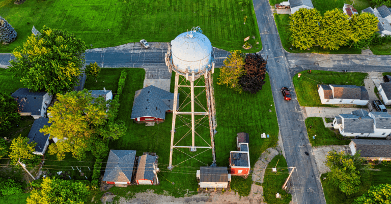 An aerial view of a water tower surrounded by farm fields and roads in a small town.