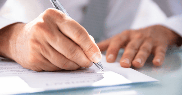 A close-up of a person's hands signing a paper document with a pen.