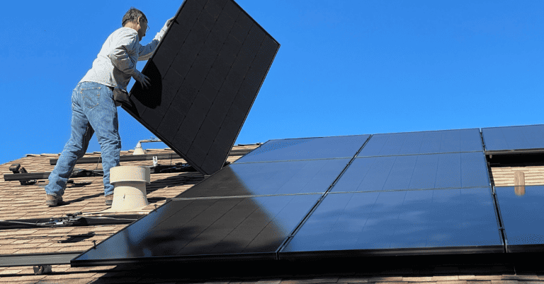 A man installing solar panels on a roof under blue skies.