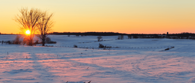 The sun is setting over a snow covered field.