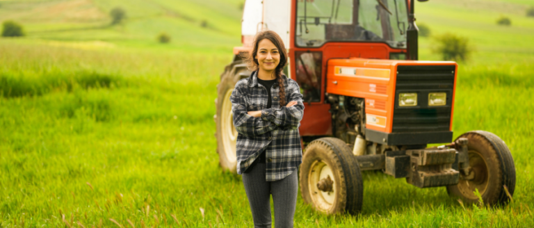 A young woman standing next to a tractor in a field.