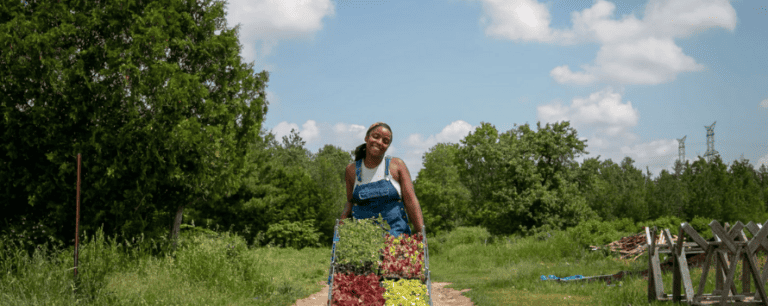 Aliyah Fraser, owner and operator of Lucky Bug Farm walking down a path showcasing vegetables and herbs (photo source: luckybugfarm.com)