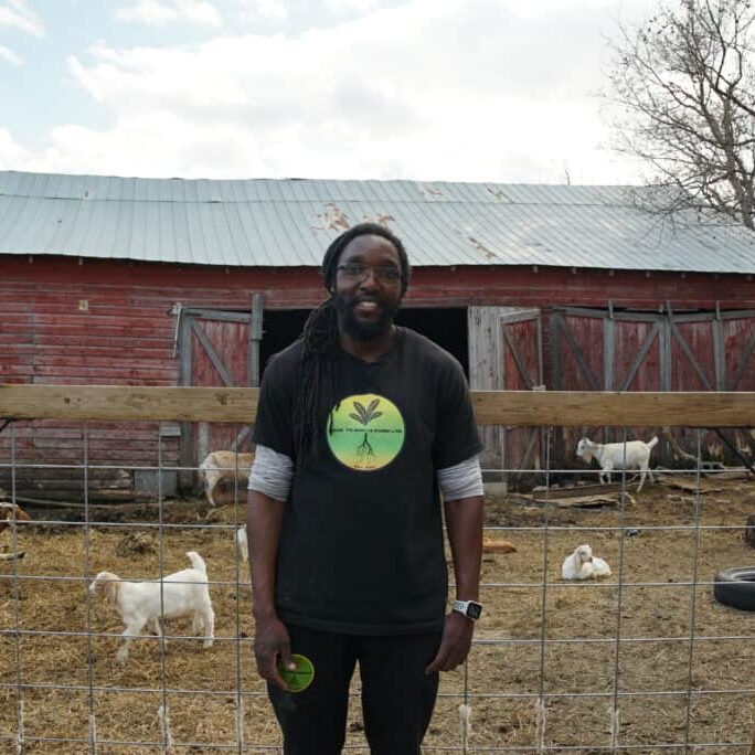 A man stands in front of a goat pen.