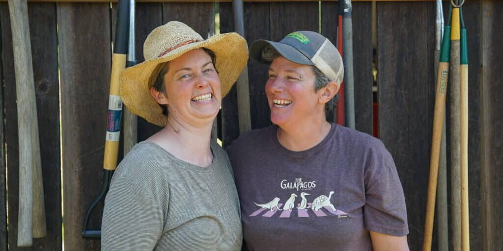 Two women smile in front of farm tools.