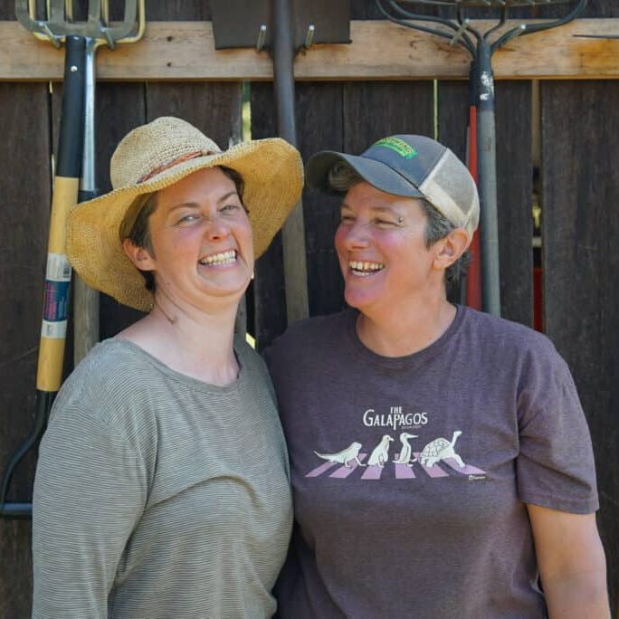 Two women smile in front of farm tools.