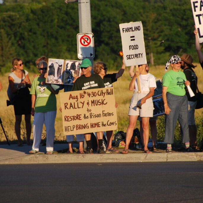 A group of people holding signs protesting the closure of Kingston's prison farm.