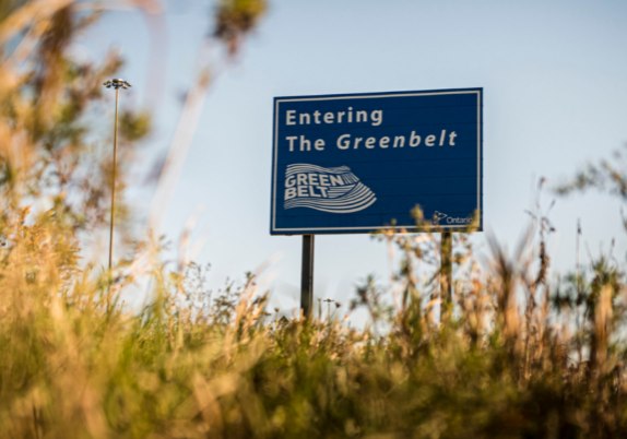 A sign that reads "Entering the Greenbelt" in a field.