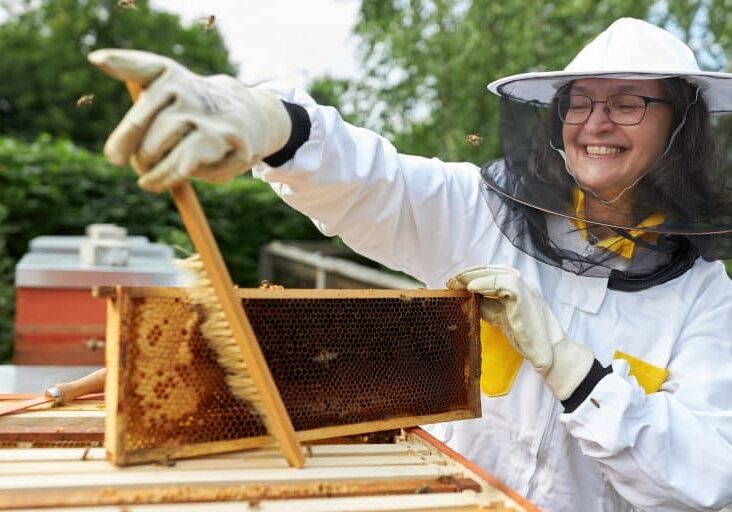 A woman in a bee suit holding a beehive.