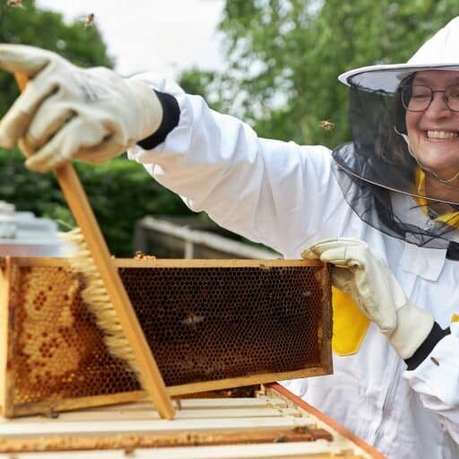 A woman in a bee suit holding a beehive.