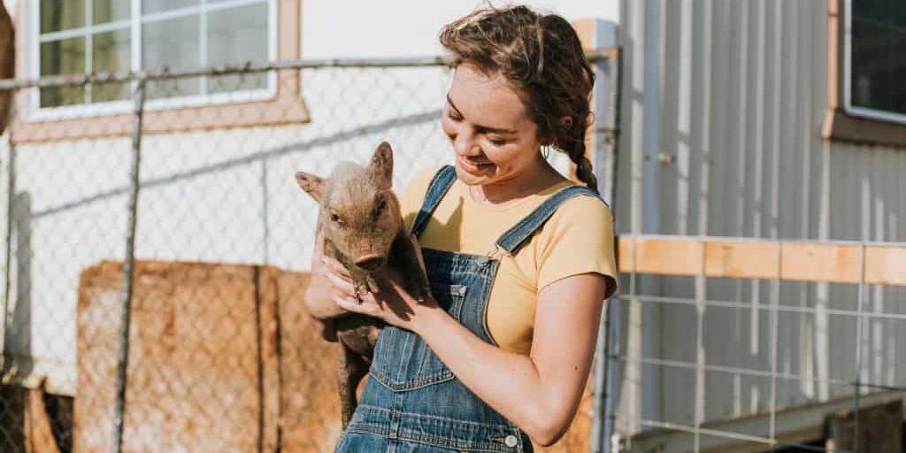 A young woman holding a pig in front of a fence.