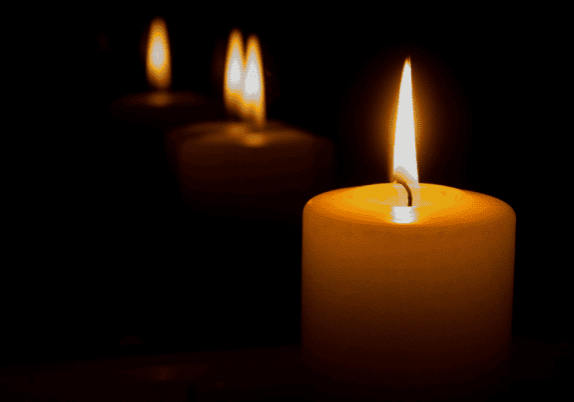 Three candles are lit in a dim room.
