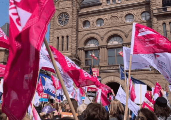 A group of people waving flags and protest signs in front of the Parliament Building in Ottawa, Ontario.