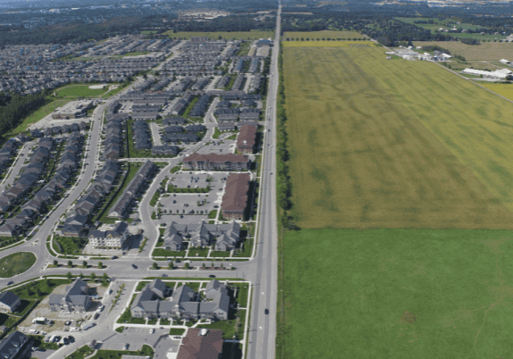 An aerial view of a residential area (left) and farmland (right) split by a road.