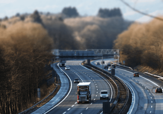 Vehicles on a six lane highway surrounded by trees on either side.