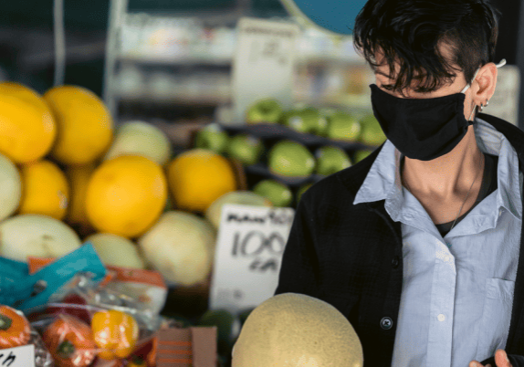 A person wearing a face mask shopping for produce in a store.