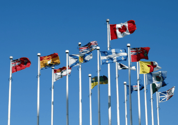 A group of flags representing countries from around the world flying in the air against a blue sky. The flag of Canada is in the forefront.