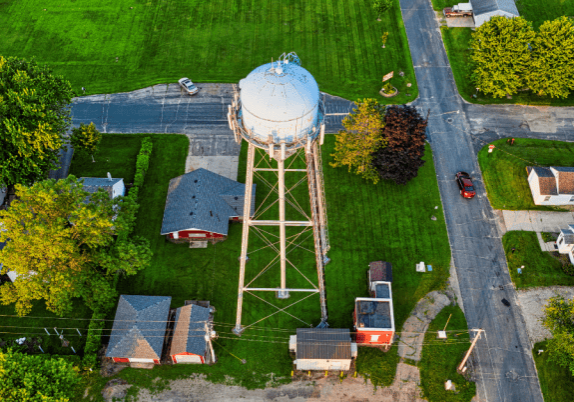 An aerial view of a water tower surrounded by farm fields and roads in a small town.