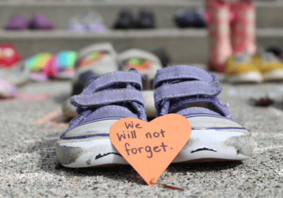 A pair of shoes with an orange heart on them that says "will we not forget you".