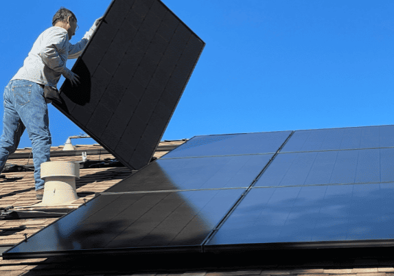 A man installing solar panels on a roof under blue skies.