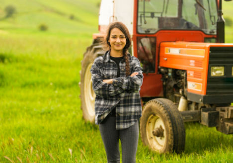 A young woman standing next to a tractor in a field.