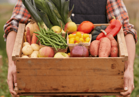 A person holding a wooden box full of vegetables.