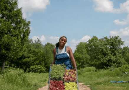 Aliyah Fraser, owner and operator of Lucky Bug Farm walking down a path showcasing vegetables and herbs (photo source: luckybugfarm.com)